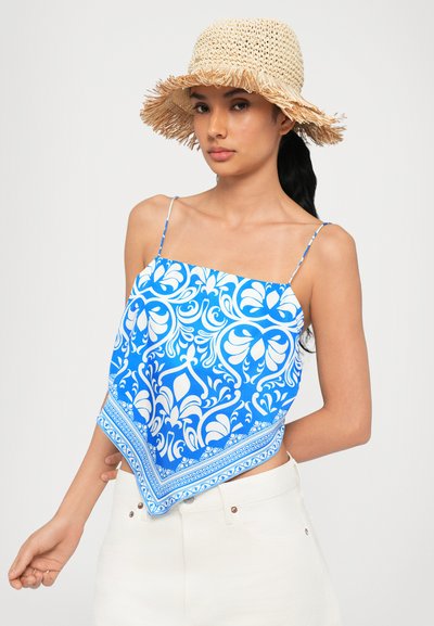 Blue patterned scarf top with white floral motifs, featuring thin straps and a triangular shape. Paired with a beige straw hat.