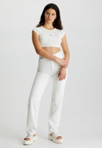Crop top alb cu dungi, cu logo, pantaloni albi cu talie înaltă și sandale albe chunky. Ținuta are un design ajustat și linii curate.