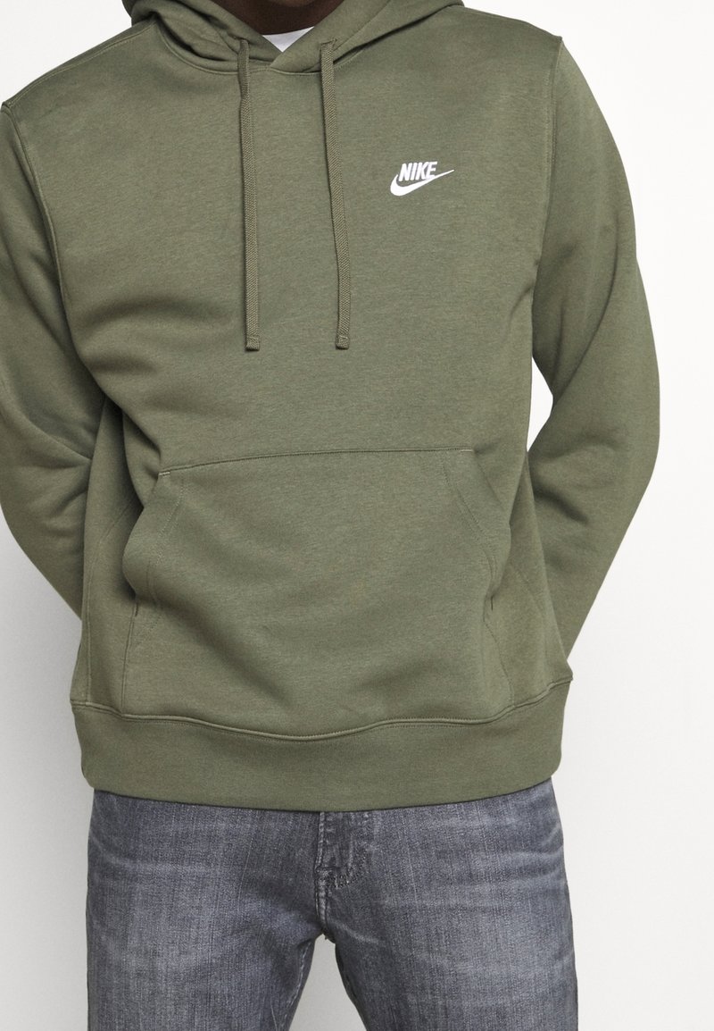 Olivgrön huva i sweatshirt-tyg av bomullsblandning med framficka och en vit Nike-logotyp på bröstet. Texturerad finish.