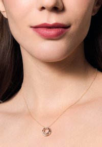 Złota naszyjnik z przeplatanymi okrągłymi zawieszkami, jedna gładka, a druga skręcona, spoczywająca na nagiej szyi.