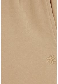 Beige szövet, texturált kötött mintával; az alsó sarokban hímzett virágdíszítéssel.