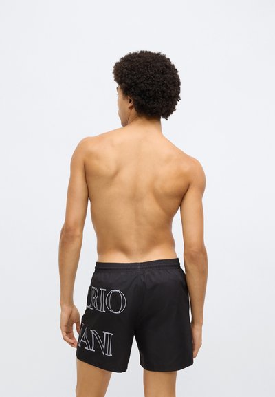 Čierne plavecké šortky s bielym nápisom na zadnej strane. Ľahký, hladký materiál, elastický pás a voľný strih.