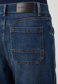 Plave traperice s tamnom kožnom etiketom s natpisom "PINKO DENIM" na struku. Dva stražnja džepa s kontrastnim narančastim šavom.