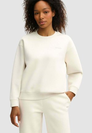 Felpa beige chiaro con collo rotondo, polsini e bordo a costine. Presenta il logo "GUESS" in rilievo sul petto. Tessuto morbido e strutturato.