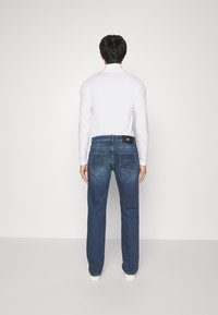 Mörkblå denimjeans med raka ben, med två bakfickor och en logopatch på midjan, som bärs med en vit långärmad tröja.