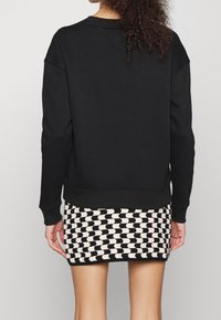 Svart sweatshirt med en texturerad mönster. Kombinerad med en minikjol med ett svart och krämfärgat geometriskt mönster. Avslappnad passform, ribbade ärmar.