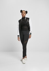 Čierno-biely varsity jacket prehozený cez čierny priliehavý top, doplnený s čiernymi legínami s priesvitnými panelmi. Biely tenisky dopĺňajú celkový vzhľad.