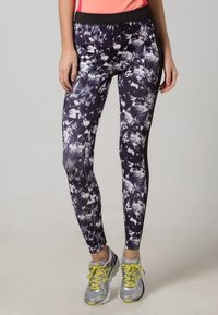 Gemusterte Leggings in dunklen Farben mit abstrakten weißen Formen; taillierte Passform mit einem breiten schwarzen Bund, kombiniert mit silbernen Laufschuhen.