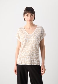 Top en tricot beige à imprimé léopard, à manches courtes et décolleté en V ; texture douce ; porté avec un pantalon noir.