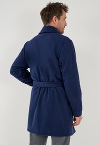 Marineblauer Fleece-Bademantel mit Schalkragen, Gürtel und langen Ärmeln. Weicher Stoff, bis zur Mitte des Oberschenkels und mit tailliertem Rücken.