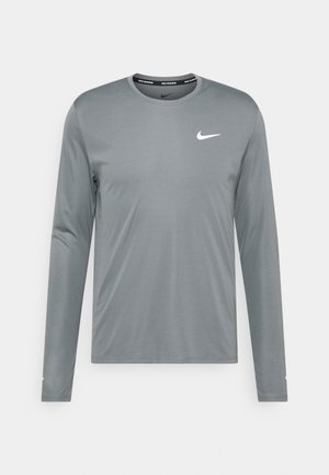 T-shirt de course Nike gris à manches longues avec col rond et logo Nike swoosh blanc sur le côté gauche de la poitrine sur fond uni.
