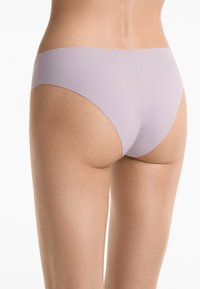 Model bevindt zich in een lichte paarse onderbroek met focus op de details van het kledingstuk. De achtergrond is neutraal.