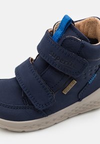 Navyblaue Knöchelboots mit zwei Klettverschlüssen, Gore-Tex-Label, strukturiertem Gummisohle und blauen Nähten. Robustes Leder.