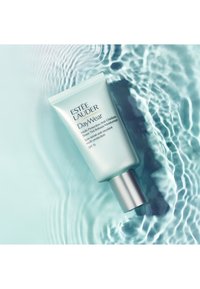 Helle grüne Tube der Estee Lauder DayWear Feuchtigkeitscreme mit silberner Kappe, versehen mit weißem Text und Logo. Auf einem Wasseroberflächen-Hintergrund platziert.