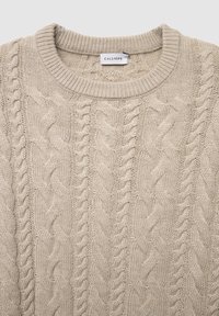 Maglione lavorato a maglia di un beige chiaro, caratterizzato da un motivo a treccia, collo rotondo e superficie testurizzata. L'etichetta riportante la scritta "CALLIOPE" è posizionata sul collo.