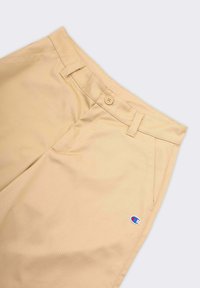 Chinos beige con una texture liscia, dotati di chiusura con bottone e tasche laterali. Distintivo piccolo logo ricamato sulla parte inferiore della gamba.