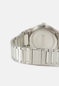 Silver stainless steel watch with a polished and brushed link bracelet, circular case, and embossed "BOSS" logo on the back.