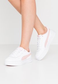 Białe sneakersy z różowymi akcentami, z gładką syntetyczną cholewką, sznurowaniem i grubą, teksturowaną podeszwą dla wsparcia.
