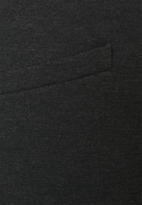 Zwarte stof met een gladde textuur en een subtiel heatherpatroon. Bevat een klein, geïntegreerd zakje op het oppervlak.