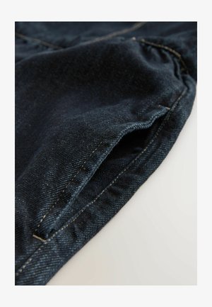 Denim tkanina u tamnoplavoj boji, s otvorom za džep s vidljivim šavovima. Tekstura izgleda blago teksturirano s glatkim završetkom.