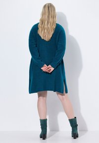 Teal stickad klänning med långa ärmar, sidoslitsar vid fållen, i kombination med gröna ankelstövlar med ett spänne.