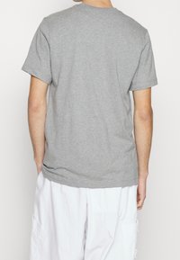 Persona vista desde atrás con una camiseta de manga corta gris lisa y pantalones cortos cargo blancos contra un fondo liso.