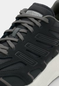 Juodas sportinis batas su tinkleliu viršuje, tekstūruotomis detalėmis ir pilkomis raišteliais. Padas baltas, kuris dar labiau išryškina kontrastą su tamsesniais medžiagomis.