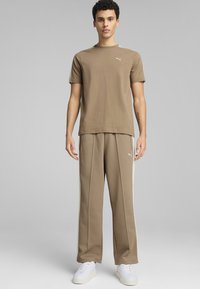 Brun bomulds T-shirt med korte ærmer og et lille logo, parret med beige træningsbukser med side-striber og hvide sneakers.