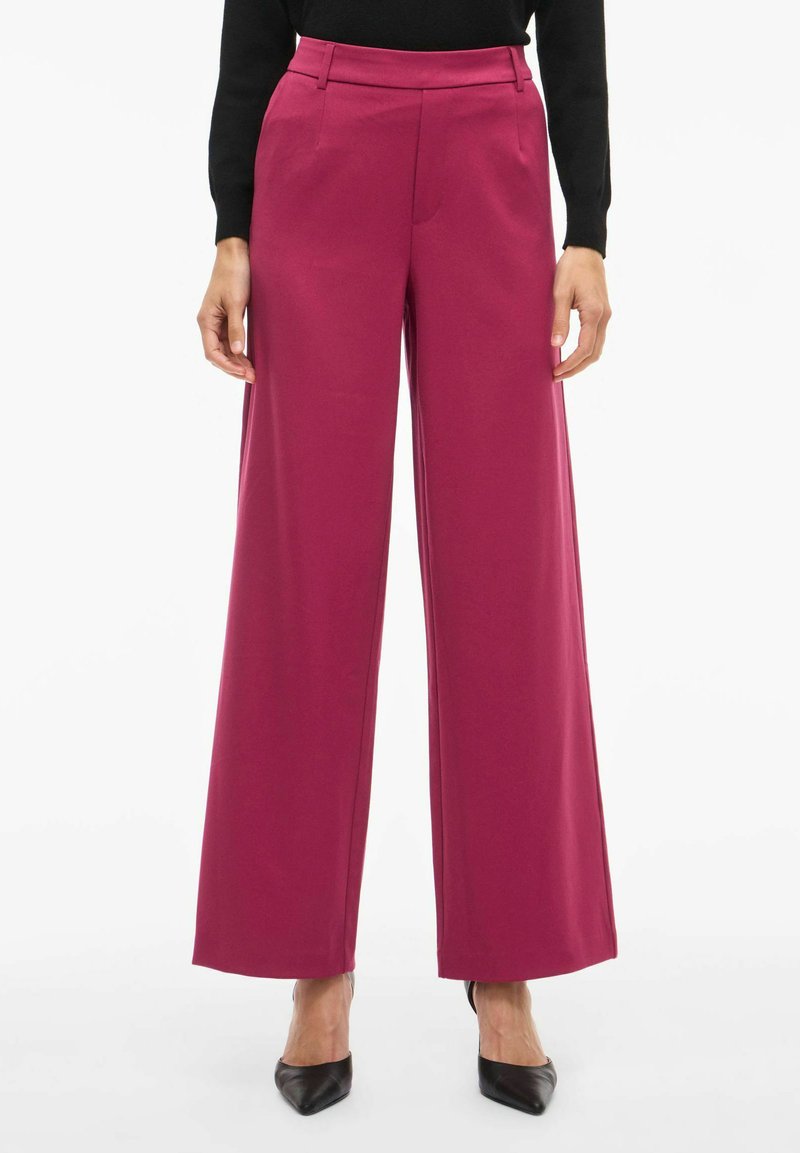 Pantalon à jambes larges de couleur magenta vif, en tissu lisse. Il présente une taille haute, un design structuré, et des poches avant.
