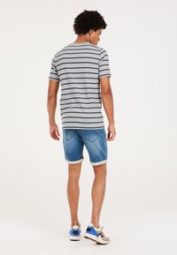 Camiseta de rayas grises con mangas cortas, combinada con pantalones cortos de mezclilla azules. Los pantalones cortos tienen puños enrollados y un detalle de bolsillo trasero.