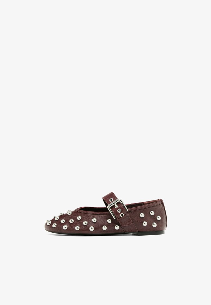 Chaussure plate en cuir bordeaux avec un bout arrondi, ornée de clous argentés et d'une bride latérale à boucle. Texture lisse avec un petit talon.