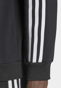 Zwarte hoodie met drie verticale witte strepen op de mouw, geribbelde manchetten en een zacht textuur. Heeft een sportief ontwerp.