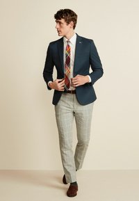 Marineblazer over en hvid skjorte, parret med grå ternede bukser og et flerfarvet slipse. Brune loafers fuldender outfittet.
