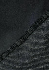 Tissu noir avec une finition lisse d'un côté et un motif texturé légèrement moucheté de l'autre ; reliés par une couture noire.