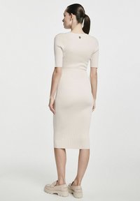 Beżowa midi sukienka o prążkowanej strukturze, z krótkimi rękawami, dopasowanym kroju oraz zapięciem na guziki z tyłu, zestawiona z masywnymi beżowymi platformami.