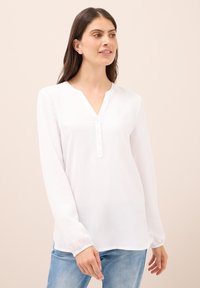 Hvid langærmet bluse med V-hals, knapdetaljer foran og elastiske manchetter, lavet af let, glat stof.