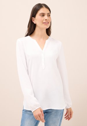Blouse blanche à manches longues avec décolleté en V, détails de boutons à l'avant et poignets élastiques, fabriquée en tissu léger et lisse.