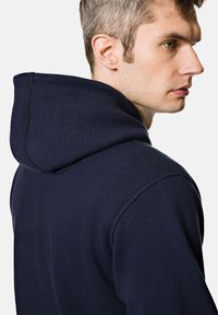 Granatowy hoodies z kapturem na sznurku, wykonany z miękkiego materiału. Posiada ribbowane mankiety i dół, prezentując swobodny i wygodny design.