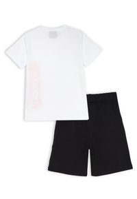 T-shirt bianca in cotone con maniche corte e un dettaglio grafico rosa sul retro, abbinata a pantaloni corti in cotone neri con vita elastica.