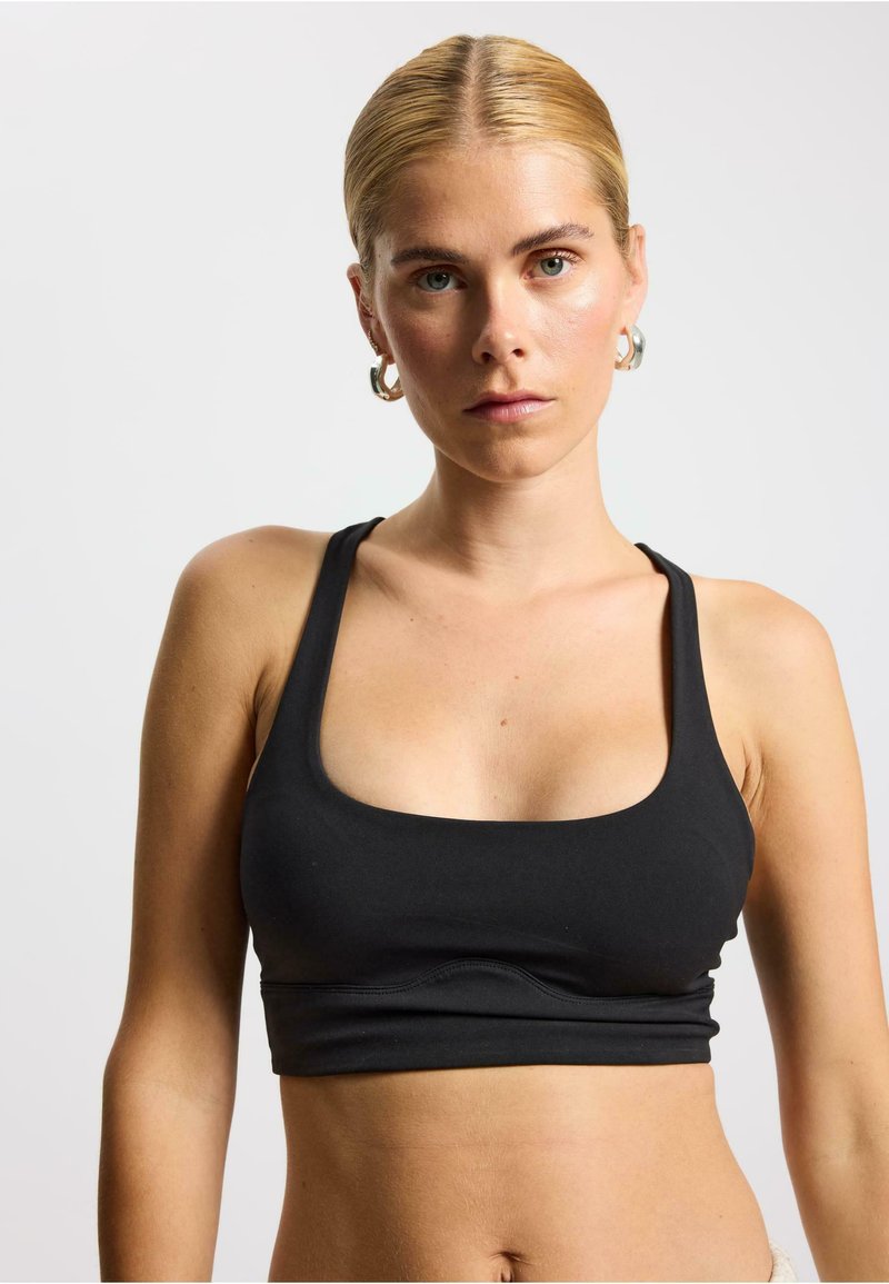 Zwarte sportbeha met een ronde halslijn en brede bandjes. Glad stof met een aansluitend ontwerp dat de lichaamsvorm benadrukt.