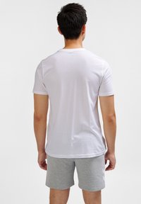Hvid bomulds t-shirt med korte ærmer, parret med grå træningsshorts med et mønstret accent på siden.