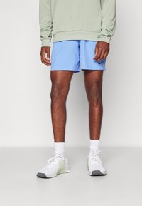Shorts de sport bleus associés à un sweat-shirt vert clair, des chaussettes blanches et des chaussures de sport grises et blanches. Logo Nike sur les shorts.