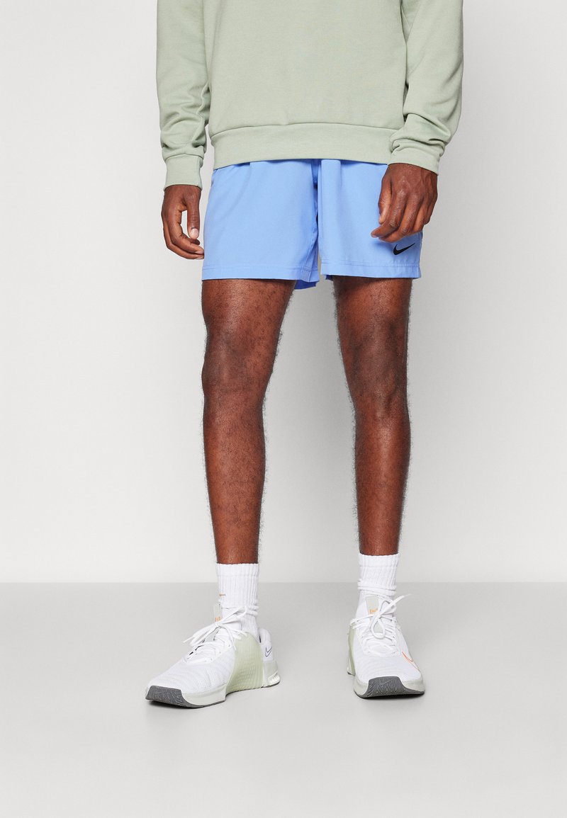 Shorts de sport bleus associés à un sweat-shirt vert clair, des chaussettes blanches et des chaussures de sport grises et blanches. Logo Nike sur les shorts.