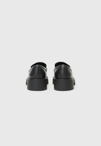 Scarpe in pelle nera con talloni arrotondati e suole spesse nere. Il design presenta cuciture minime e una consistenza liscia.