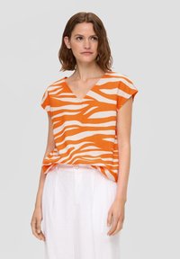 Oranje en crèmekleurige gestreepte blouse met een V-hals en kapmouwen, gemaakt van lichte stof, gecombineerd met witte linnen broek.