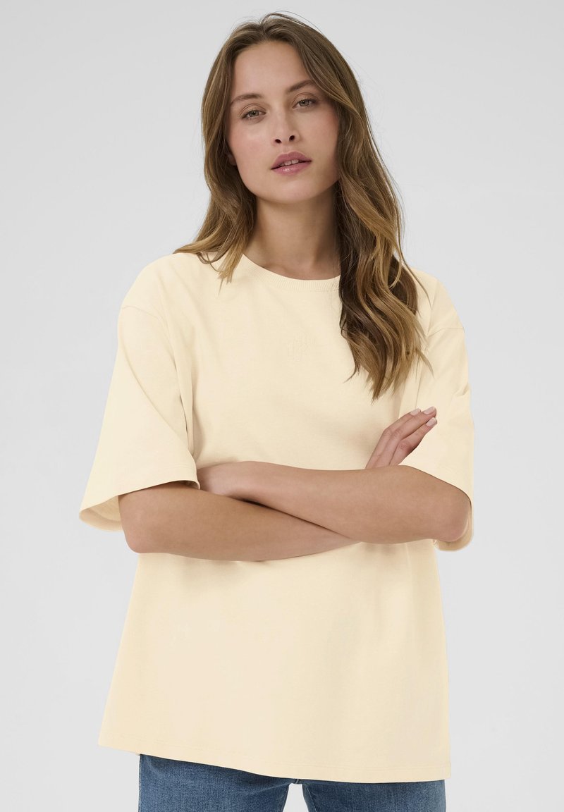 T-shirt court à manches courtes de couleur jaune clair avec un col rond et une coupe décontractée, fabriqué en tissu doux, présentant un logo subtil à l'avant.