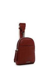 Červená kožená crossbody taška s texturovaným povrchem, zaobleným tvarem, stříbrnými zipy a kontrastním pruhovaným nastavitelným popruhem.