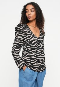 Langärmliges Oberteil mit V-Ausschnitt und Puffärmeln, in einem schwarzen und beigen Zebra-Druckmuster auf strukturiertem Stoff.