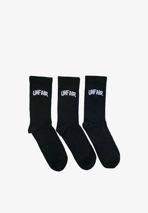 Drei Paare schwarze Knöchelsocken nebeneinander, jeweils mit dem Wort "UNFAIR" in weißer Schrift nahe der Oberseite.
