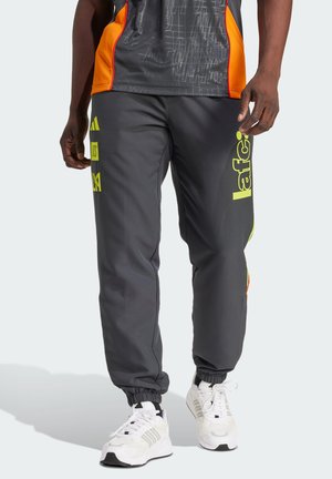 Grijze sportbroek met een taps toelopende pasvorm, getailleerde boorden, neon gele branding en oranje accenten aan de zijkanten. Gecombineerd met witte sneakers.